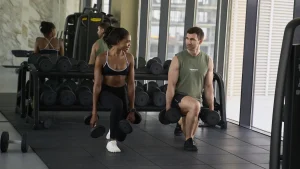 Personal trainer Rozzie Kinyua and a male client performing dumbbell lunges together in a Dubai gym.