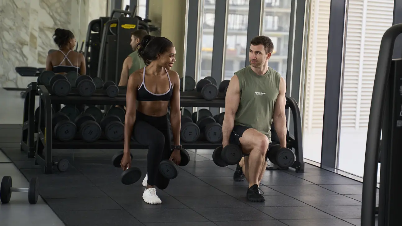 Personal trainer Rozzie Kinyua and a male client performing dumbbell lunges together in a Dubai gym.