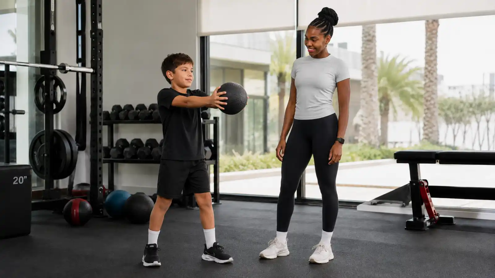 Young boy doing a medicine ball exercise with a female trainer during a supervised kids strength training session in Dubai.